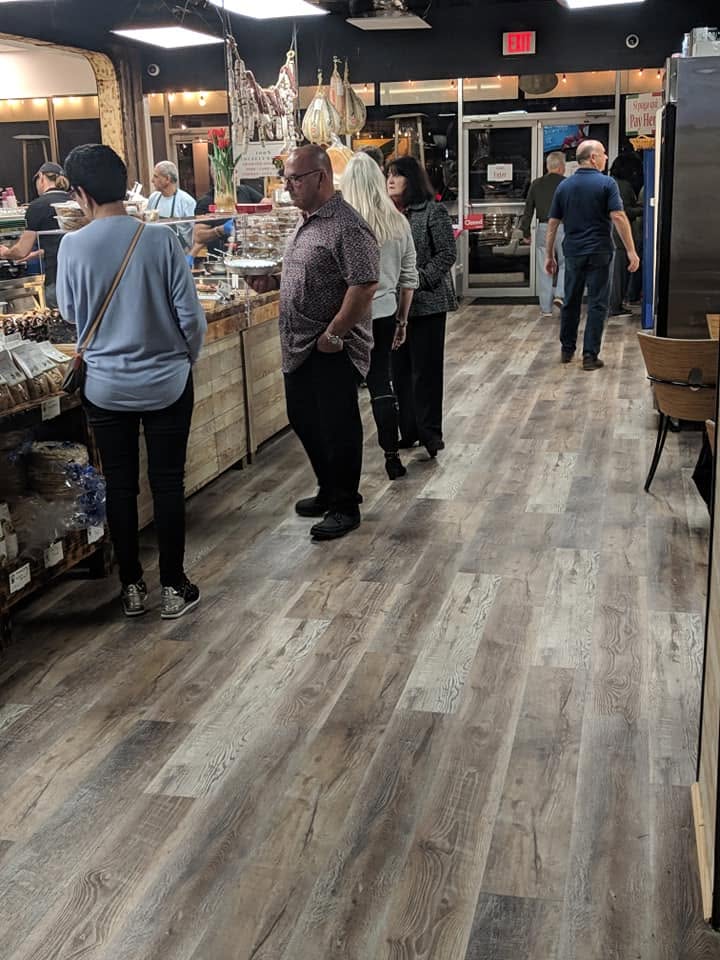 Customers waiting in line along the food counter inside a deli.