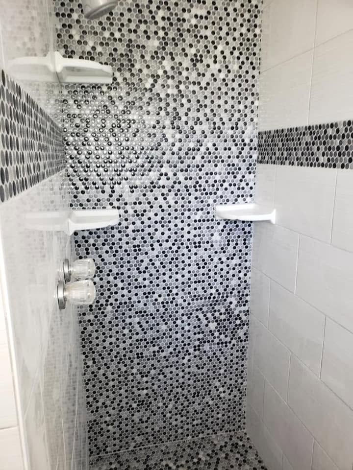 Shower stall featuring black and white penny round mosaic tile and corner shelves.