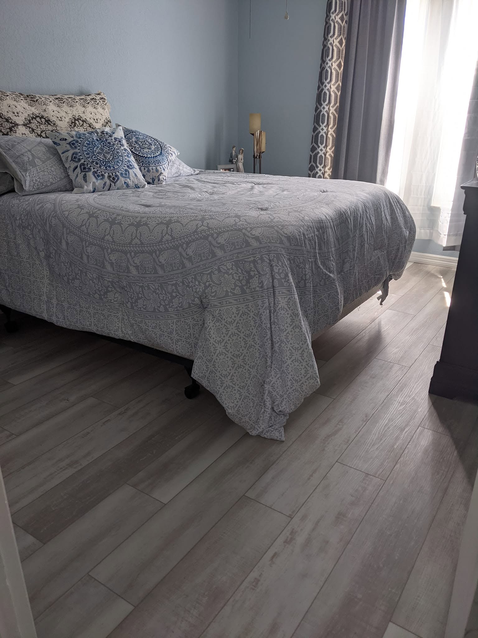 Light wood-look laminate flooring in a bright bedroom beside a made bed.