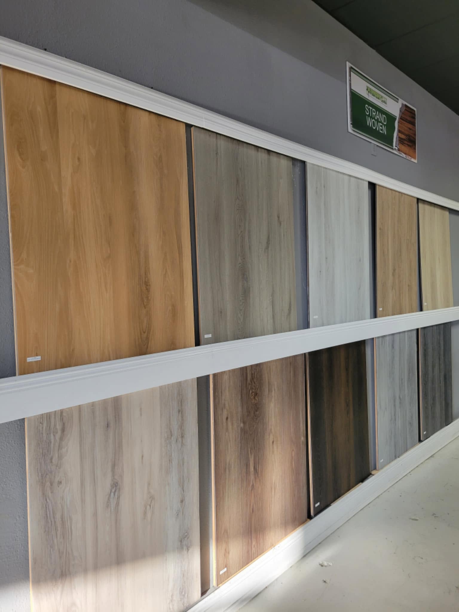 Various wood-look flooring samples displayed on a showroom wall in two rows.