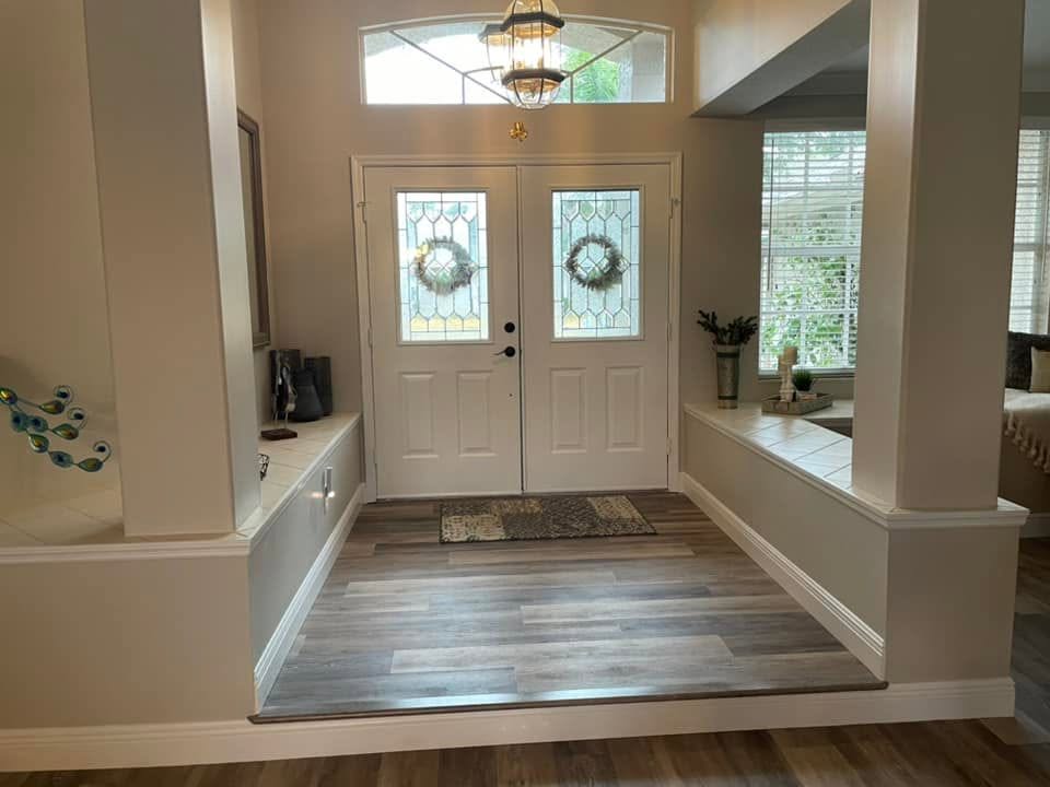 A bright home entryway features wood-look plank flooring and white double front doors.