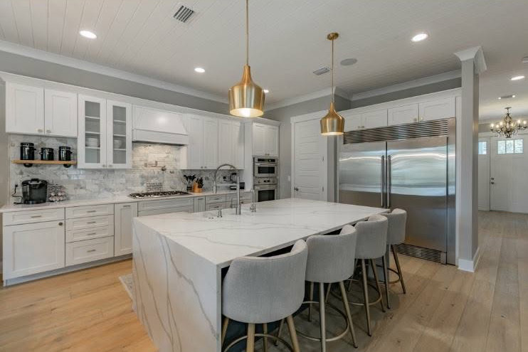 Modern kitchen with white cabinets, a large marble island, and gold pendant lights.