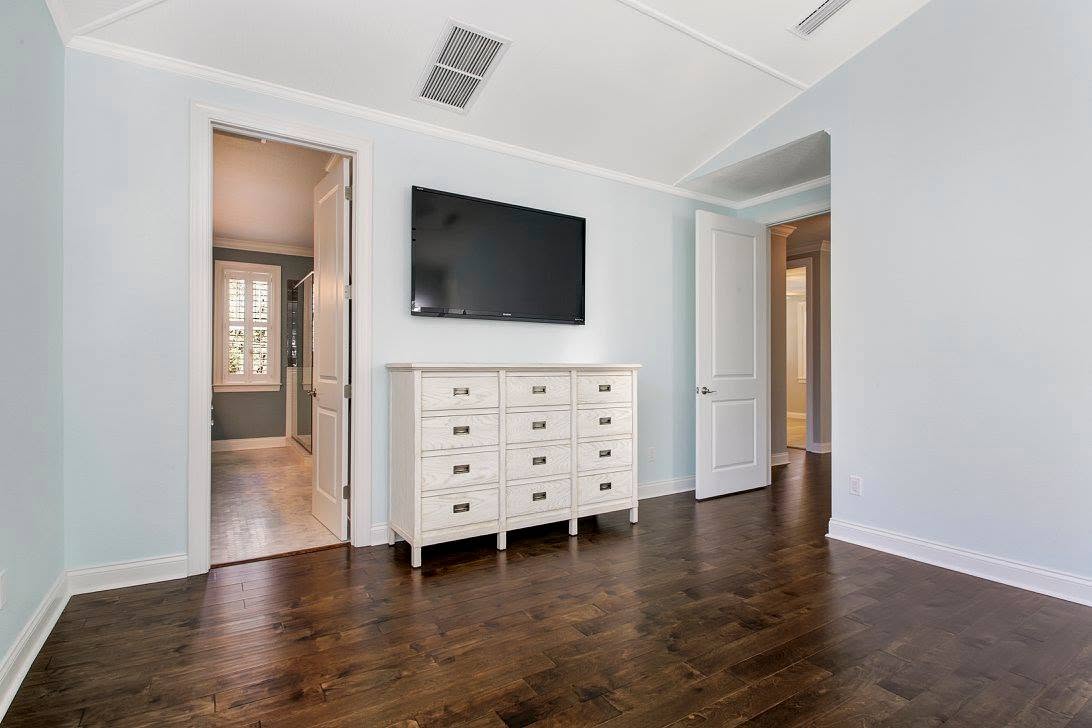 Dark hardwood flooring in a pale blue room with white dresser and wall-mounted television.