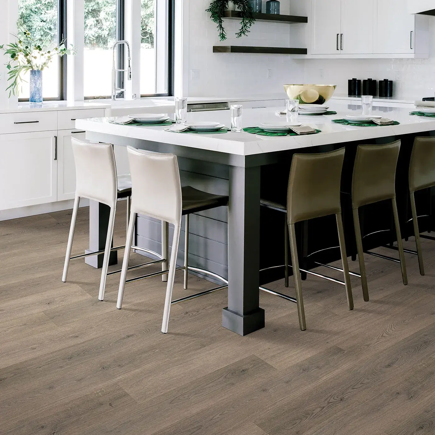 White kitchen with large island, upholstered bar stools, and brown wood-look flooring.