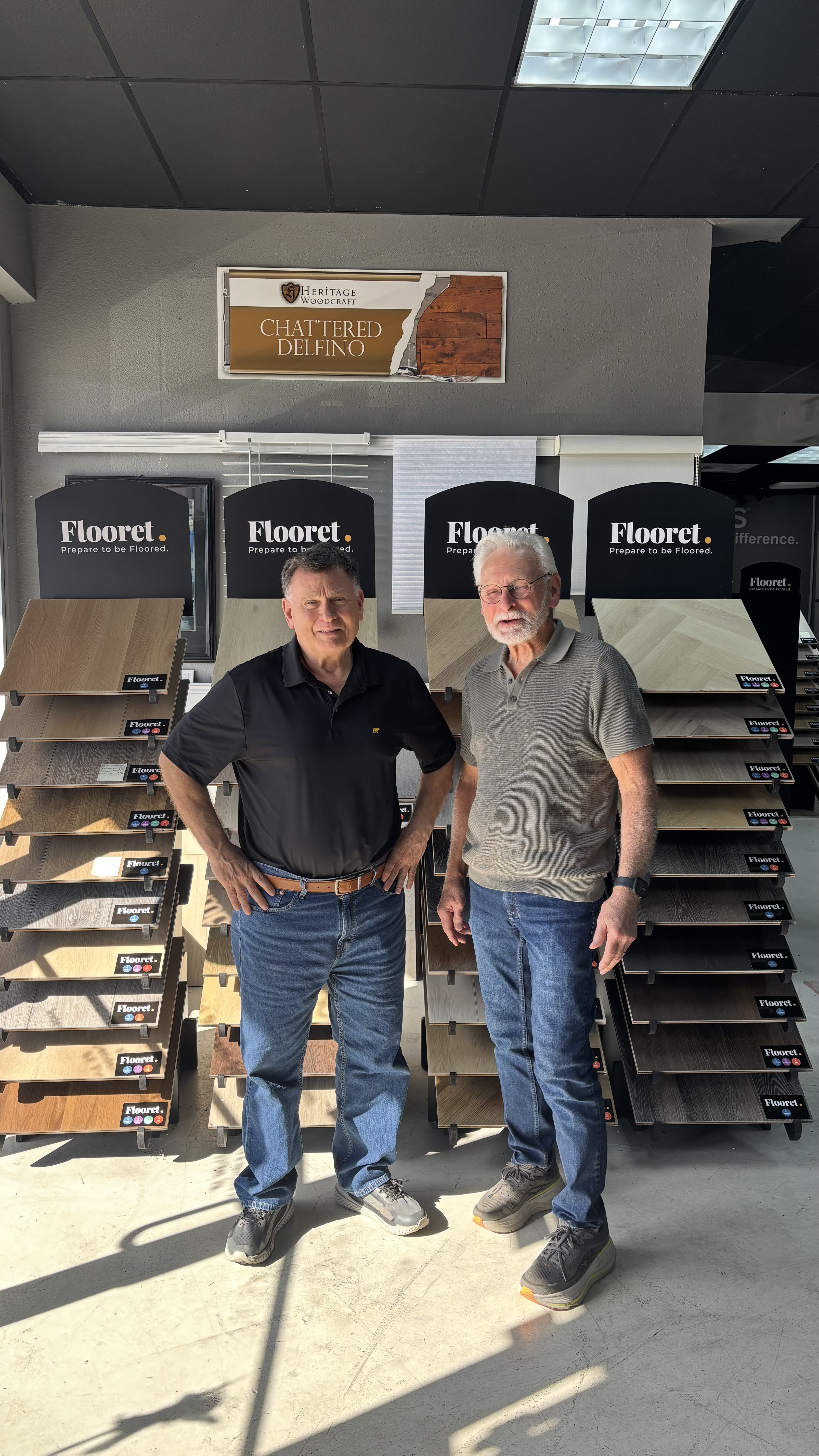 Two men standing in front of sample flooring displays inside a showroom.