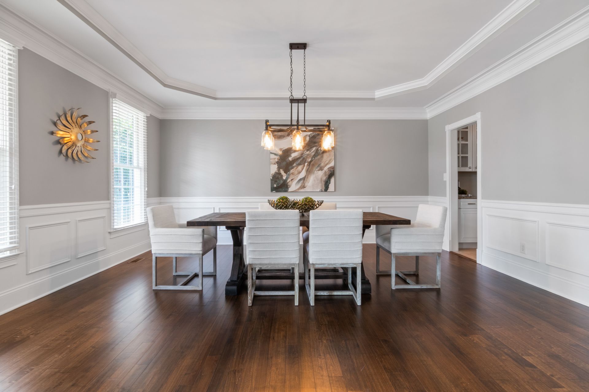 Dining room with dark hardwood flooring, wooden table, upholstered chairs, and hanging lights.
