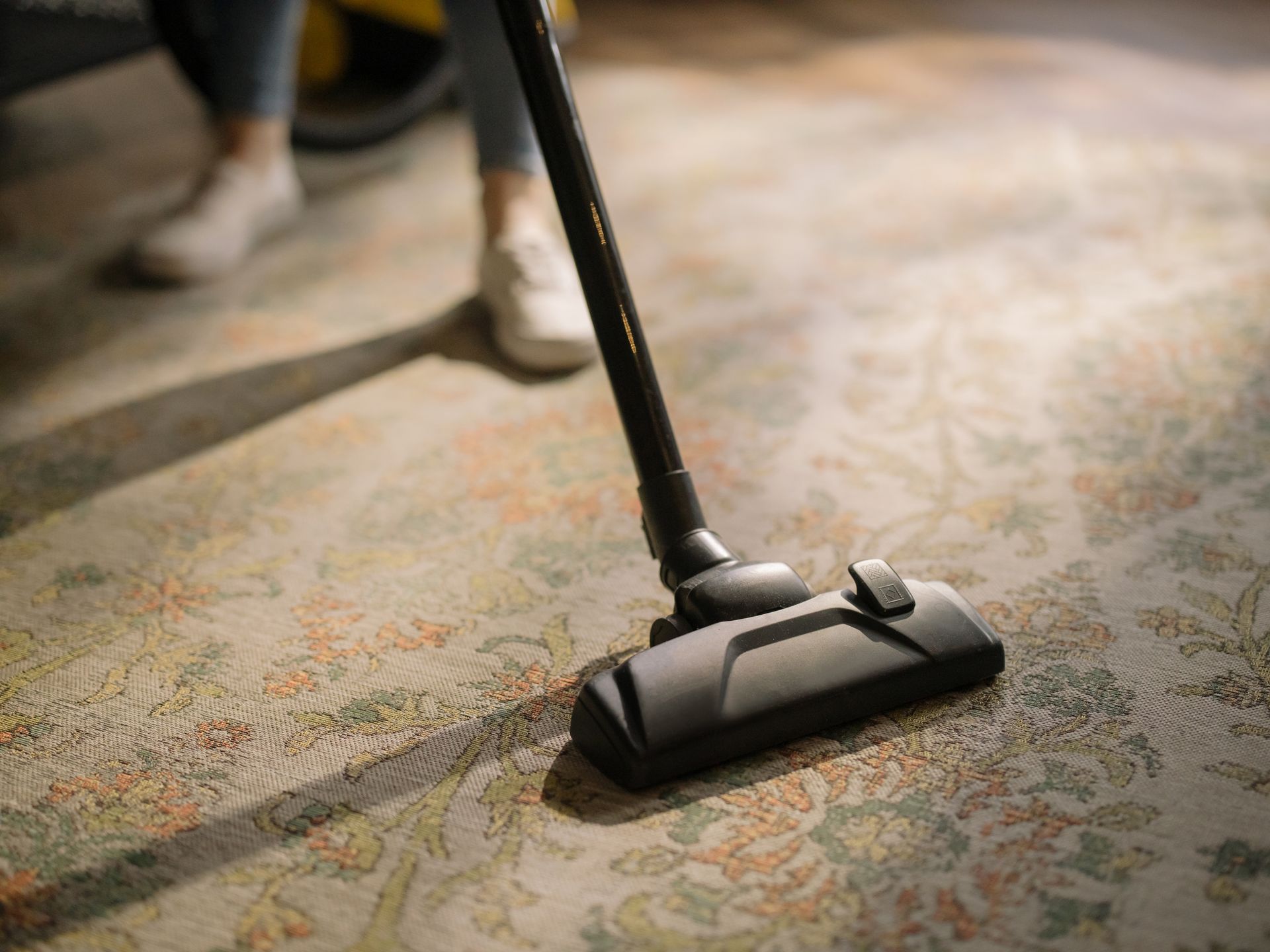 A person cleans an ornate patterned rug with a vacuum cleaner.
